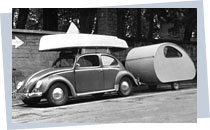 Ein Volkswagen-Käfer mit einem Segelboot auf dem Dachgepäckträger und einem kleinen angekoppelten Wohnwagen; Rechte: dpa 