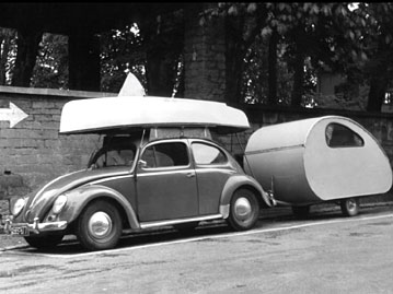 Ein Volkswagen-Käfer mit einem Segelboot auf dem Dachgepäckträger und einem kleinen angekoppelten Wohnwagen; Rechte: dpa